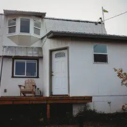 Small white house with front deck and chairs in Fairbanks, Alaska—ideal for treehouse-style rental or lodge getaway