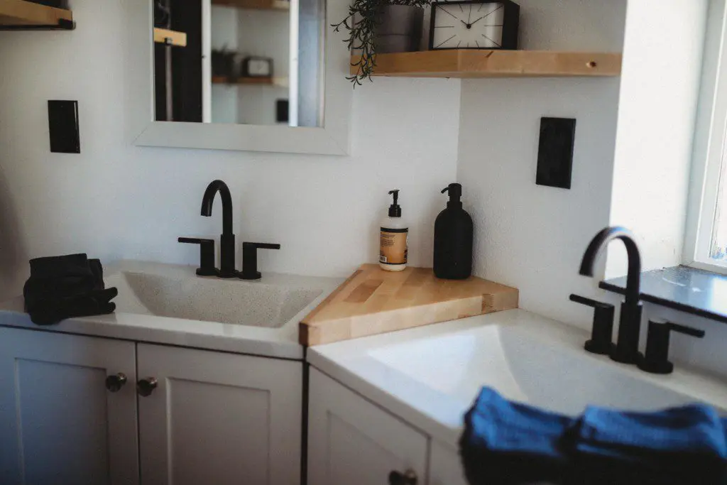 Bright modern bathroom with dual sinks, black matte faucets, and wooden shelves in a Fairbanks treehouse