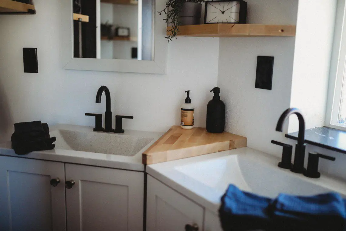 Bright modern bathroom with dual sinks, black matte faucets, and wooden shelves in a Fairbanks treehouse