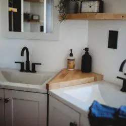 Bright modern bathroom with dual sinks, black matte faucets, and wooden shelves in a Fairbanks treehouse