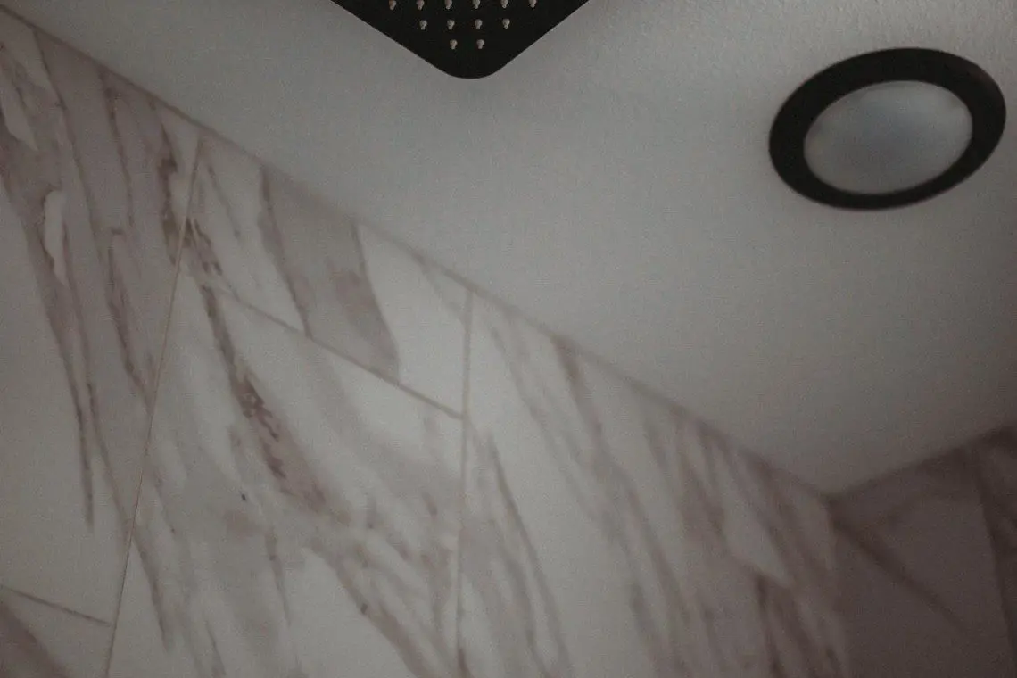 Overhead rain showerhead with marble-style wall in Alaska adventure treehouse bathroom  Caption: