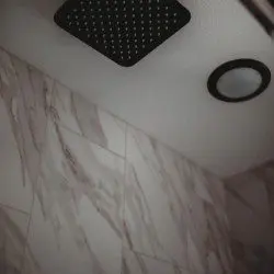 Overhead rain showerhead with marble-style wall in Alaska adventure treehouse bathroom  Caption: