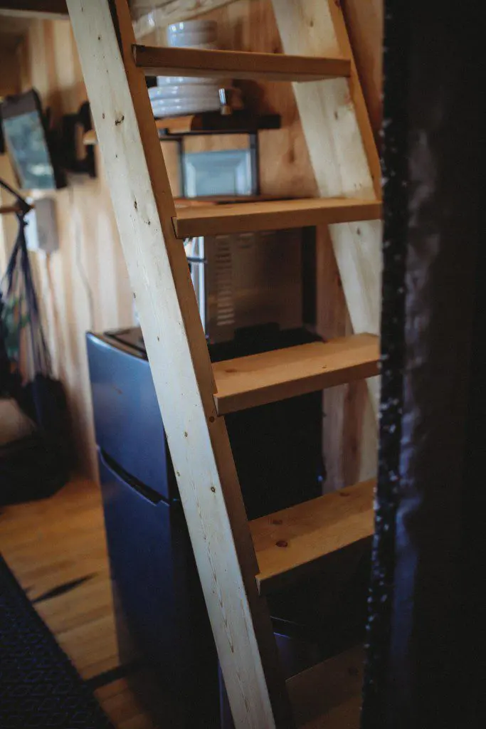 Wooden ladder above mini fridge inside a cozy treehouse rental in Fairbanks Alaska