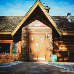 Front view of a rustic log cabin with wooden door, pitched roof, and snow-dusted walkway in Fairbanks, Alaska
