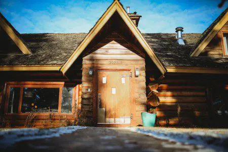 Front view of a rustic log cabin with wooden door, pitched roof, and snow-dusted walkway in Fairbanks, Alaska