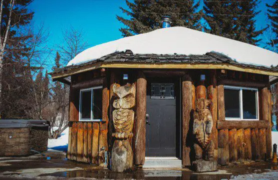 Rustic round wooden cabin with carved totem pillars and snowy roof in Fairbanks Alaska