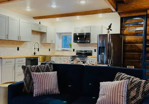 Stylish kitchen with white cabinets and navy couch in a rustic Fairbanks Alaska treehouse rental