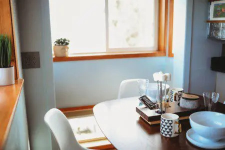 Small dining table with mugs, books, and white chairs by a sunny window in a Fairbanks Alaska treehouse