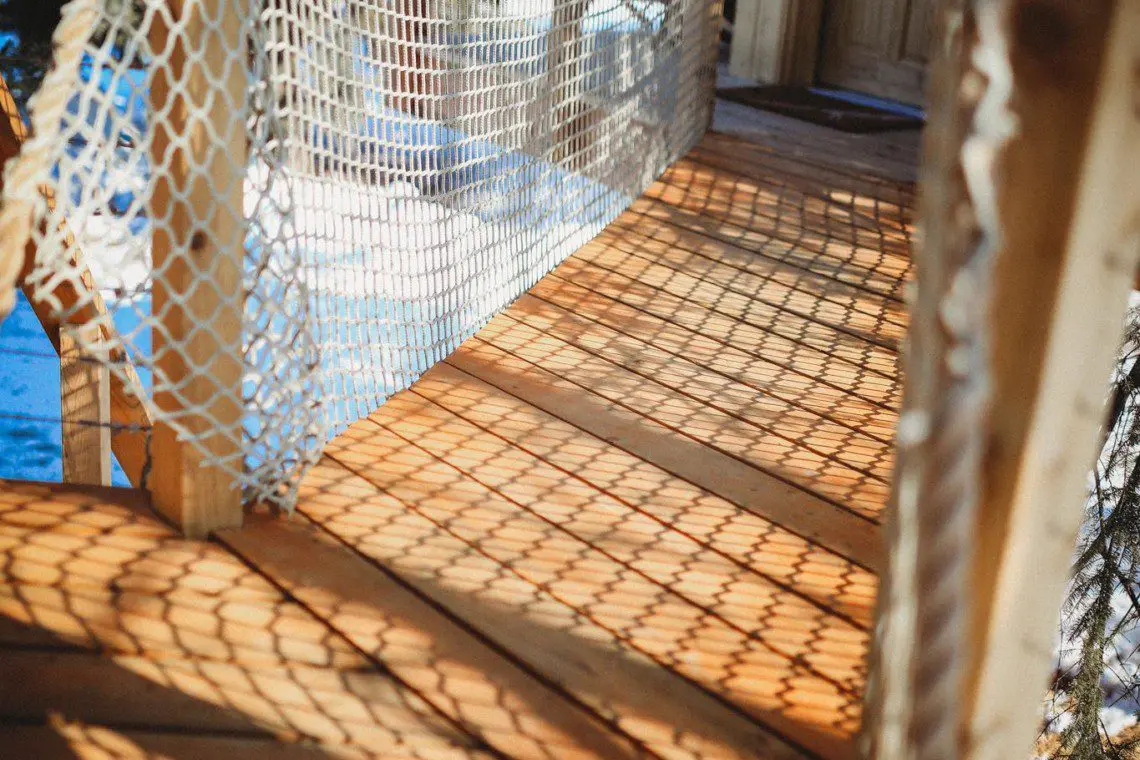 Wooden rope bridge with netted sides and sun shadows at a Fairbanks Alaska treehouse rental