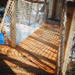 Wooden rope bridge with netted sides and sun shadows at a Fairbanks Alaska treehouse rental