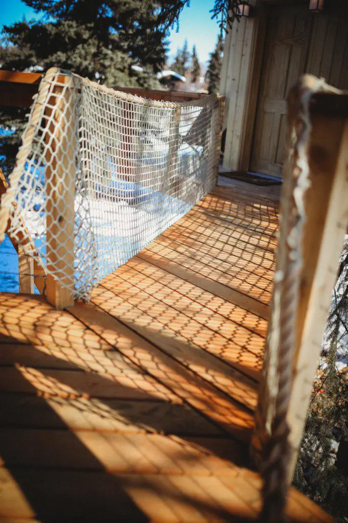 Wooden rope bridge with netted sides and sun shadows at a Fairbanks Alaska treehouse rental