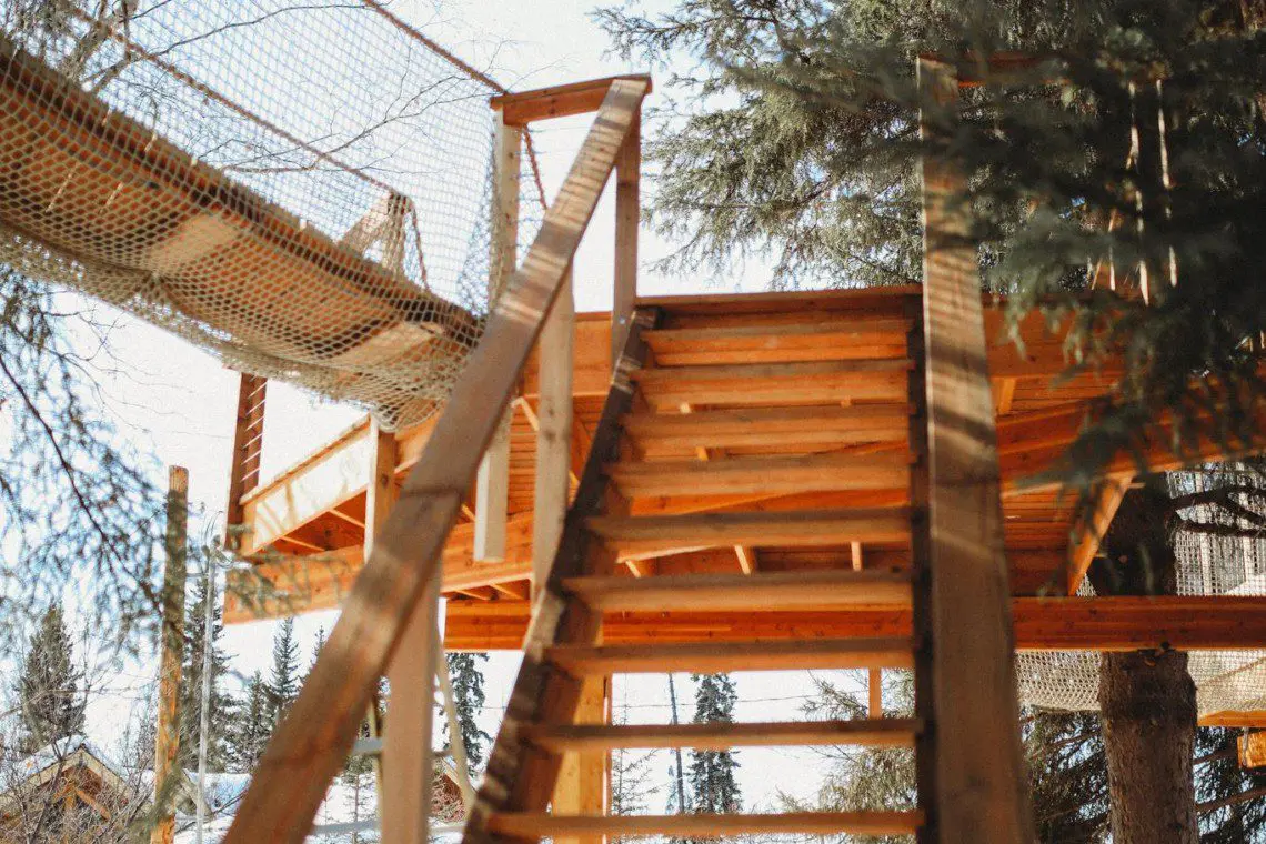 Wooden stairs leading up to a rope bridge and treehouse in snowy Fairbanks Alaska forest