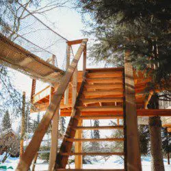 Wooden stairs leading up to a rope bridge and treehouse in snowy Fairbanks Alaska forest