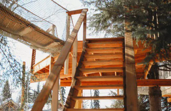 Wooden stairs leading up to a rope bridge and treehouse in snowy Fairbanks Alaska forest