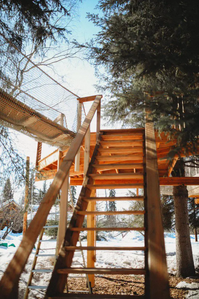 Wooden stairs leading up to a rope bridge and treehouse in snowy Fairbanks Alaska forest