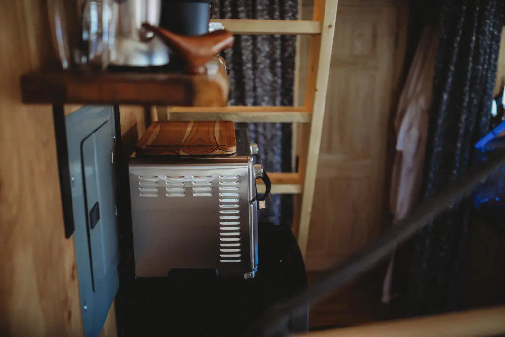 Small kitchen setup with appliances, shelves, and curtain in a rustic Fairbanks Alaska treehouse rental