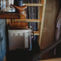 Small kitchen setup with appliances, shelves, and curtain in a rustic Fairbanks Alaska treehouse rental
