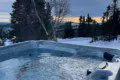 Outdoor hot tub filled with water surrounded by snow and overlooking a forested landscape in Fairbanks, Alaska