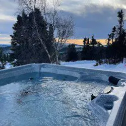 Outdoor hot tub filled with water surrounded by snow and overlooking a forested landscape in Fairbanks, Alaska