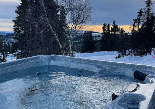 Outdoor hot tub filled with water surrounded by snow and overlooking a forested landscape in Fairbanks, Alaska