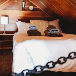 Cozy loft bed with folded towels and wood-paneled walls in Fairbanks Alaska treehouse