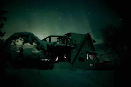 Nighttime view of a cozy treehouse structure under glowing green northern lights in Fairbanks, Alaska