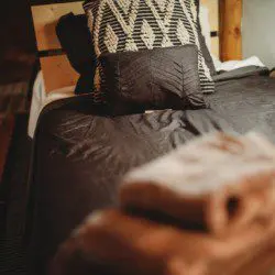 Bed with dark linens, patterned pillows, and folded towels in a Fairbanks Alaska treehouse rental