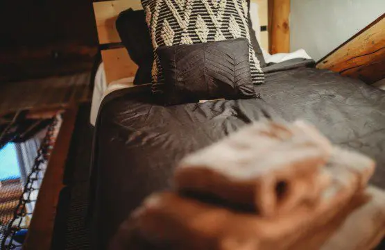 Bed with dark linens, patterned pillows, and folded towels in a Fairbanks Alaska treehouse rental