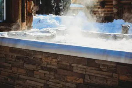 Steaming outdoor hot tub beside a log cabin in snowy Fairbanks Alaska