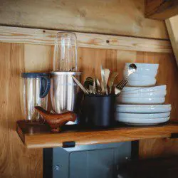 Wood shelf with plates, utensils, and blender in a cozy Fairbanks Alaska treehouse rental kitchen