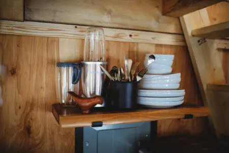 Wood shelf with plates, utensils, and blender in a cozy Fairbanks Alaska treehouse rental kitchen