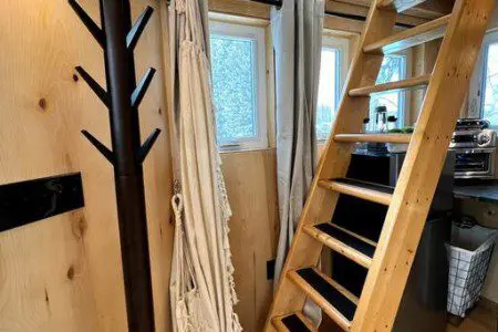 Wooden ladder leading to loft beside windows and kitchenette in Fairbanks Alaska treehouse