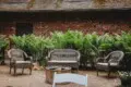 Wicker seating around a firepit on a brick patio with lush greenery and a rustic brick wall in Fairbanks, Alaska