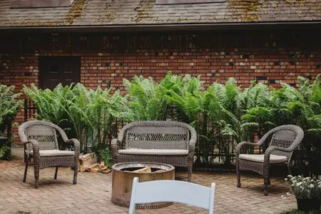 Wicker seating around a firepit on a brick patio with lush greenery and a rustic brick wall in Fairbanks, Alaska