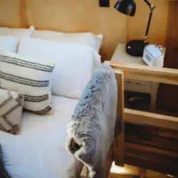 Made bed with soft pillows, gray towels, and sunlight streaming through windows in Fairbanks treehouse