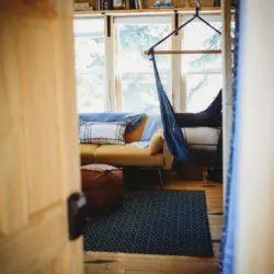 Interior view of a sunlit room with hammock chair, sofa, and pouf in a Fairbanks Alaska treehouse rental