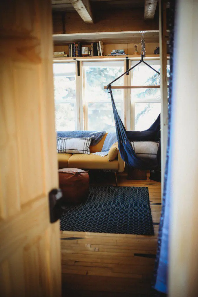 Interior view of a sunlit room with hammock chair, sofa, and pouf in a Fairbanks Alaska treehouse rental