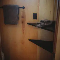 Small bathroom area with wooden walls, towel rack, and folded towels on corner shelves in Fairbanks treehouse