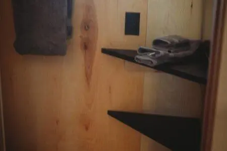 Small bathroom area with wooden walls, towel rack, and folded towels on corner shelves in Fairbanks treehouse