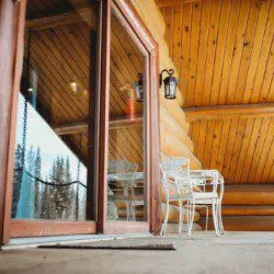 Covered log cabin deck with metal chairs and forest view reflection in Fairbanks Alaska