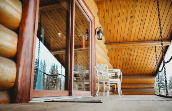 Covered log cabin deck with metal chairs and forest view reflection in Fairbanks Alaska