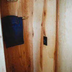 Small wood-paneled closet area with towel hanging on a brass hook in a Fairbanks Alaska treehouse rental  Caption: