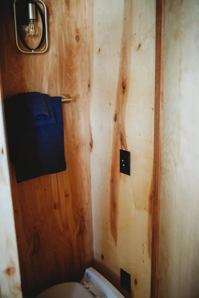 Small wood-paneled closet area with towel hanging on a brass hook in a Fairbanks Alaska treehouse rental  Caption:
