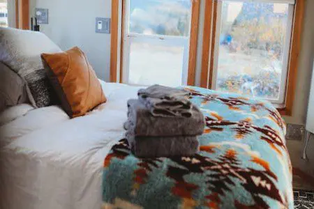 Cozy bed with folded towels and colorful blanket near large windows in a Fairbanks Alaska treehouse