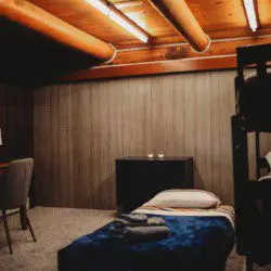 Warmly lit guest bedroom with single bed, wood ceiling beams, and cozy decor in a Fairbanks Alaska treehouse rental