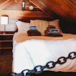 Bottle of champagne and glasses on bed with patterned blanket in cozy Fairbanks treehouse rental