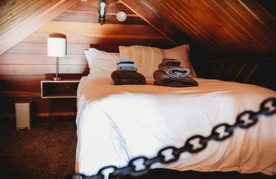 Bottle of champagne and glasses on bed with patterned blanket in cozy Fairbanks treehouse rental
