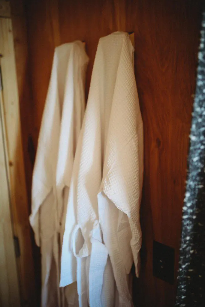 Two soft white robes hanging on wooden wall in a Fairbanks Alaska lodge or treehouse rental