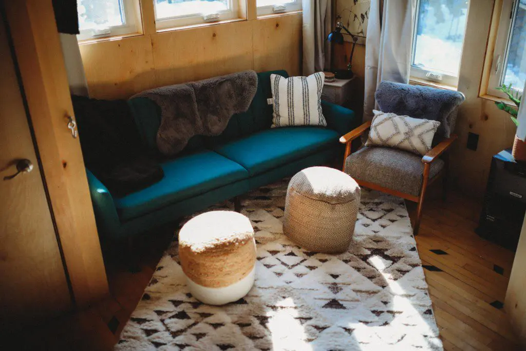 Cozy treehouse living room with teal couch, accent pillows, woven poufs, and large windows in Fairbanks, Alaska