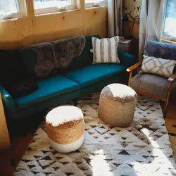 Cozy treehouse living room with teal couch, accent pillows, woven poufs, and large windows in Fairbanks, Alaska